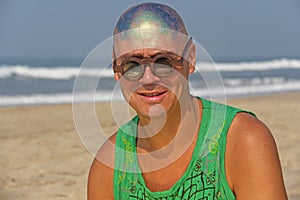 A bald and unusual young man, a freak, with a shiny bald head and round wooden glasses on the background of the beach and the sea