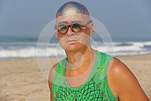 A bald and unusual young man, a freak, with a shiny bald head and round wooden glasses on the background of the beach and the sea