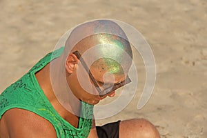 A bald and unusual young man, a freak, with a shiny bald head and round wooden glasses on the background of the beach and the sea