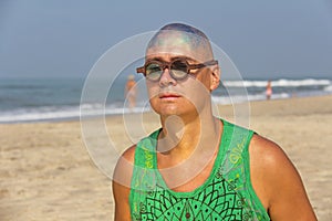 A bald and unusual young man, a freak, with a shiny bald head and round wooden glasses on the background of the beach and the sea