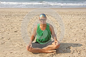 A bald and unusual young man, a freak, with a shiny bald head and round wooden glasses on the background of the beach and the sea