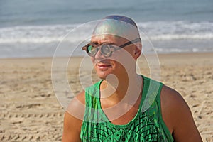 A bald and unusual young man, a freak, with a shiny bald head and round wooden glasses on the background of the beach and the sea