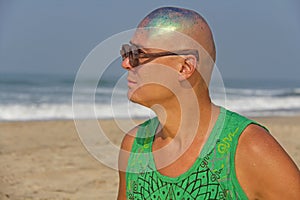 A bald and unusual young man, a freak, with a shiny bald head and round wooden glasses on the background of the beach and the sea