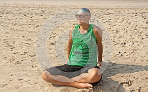 A bald and unusual young man, a freak, with a shiny bald head and round wooden glasses on the background of the beach and the sea