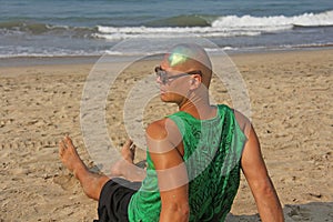 A bald and unusual young man, a freak, with a shiny bald head and round wooden glasses on the background of the beach and the sea