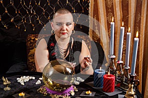 A bald woman fortuneteller reads the future on runes by candlelight in a magic salon.