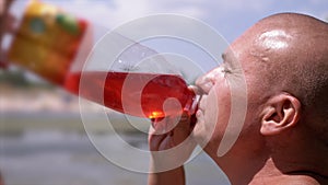 Bald Wrinkly Man Greedily Drinks Juice, Drink, Colored Water Against the Sky