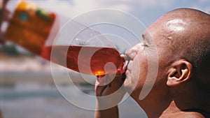 Bald Wrinkly Man Greedily Drinks Juice, Drink, Colored Water Against the Sky