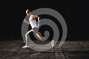 Bald young athletic tattooed man running fast outdoor, sportsman preparing to marathon, doing cardio exercises