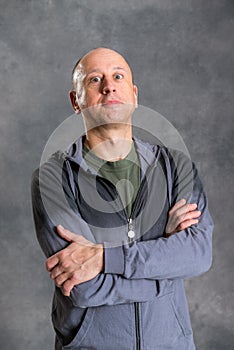 Baldheaded man with crossed arms in front of gray background