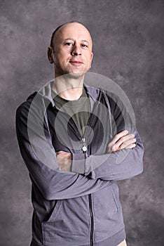 Baldheaded man with crossed arms in front of gray background