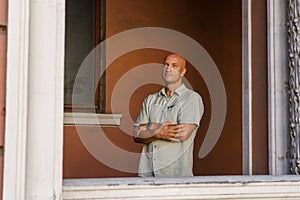 A balding middle-aged man in a plaid shirt stands against a painted wall