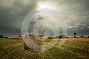 A bale of hay in the meadow and the glow of the sun from behind grey clouds