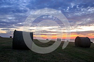 Bales of harvested wheat on the cliff edge during sunset