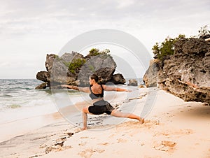 Bali beach yoga. Caucasian woman practicing Virabhadrasana II, Warrior II Pose. Strong body. Healthy lifestyle. View from back.