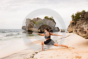 Bali beach yoga. Caucasian woman practicing Virabhadrasana II, Warrior II Pose. Strong body. Healthy lifestyle. View from back.