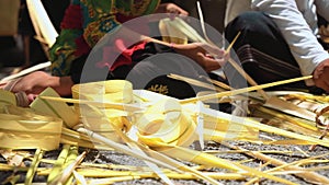 Balinese man and woman making palm leaf decorations for a penjor on Galungan, close up