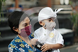 Balinese mother and child are wearing Balinese traditional clothes during the corona pandemic or covid-19. They both use masks to