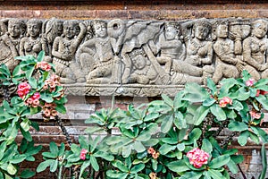 Balinese stone carving on the wall near blooming Euphorbia milii plant. Bali, Indonesia.