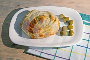 Balkan cuisine. Burek - popular national dish. Round burek on a white plate, rustic background