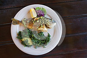 Balkan cuisine. Grilled fish  sea bream  with green leafy vegetables on white plate. Flat lay