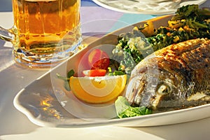 Balkan cuisine. Sunday lunch: mug of beer and grilled fish with vegetables
