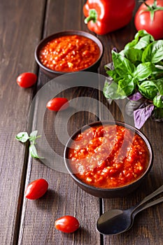 Balkan sauce ajvar in a clay bowl and ingredients for its preparation on a wooden background. Serbian traditional food