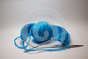 A ball of blue yarn on a white background with knitting needles