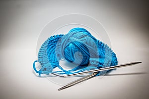 A ball of blue yarn on a white background with knitting needles