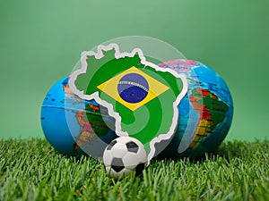 Ball and brazil flag sticker on a green field with a blurred globe behind it.