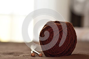 A ball of brown woolen threads and two wooden knitting needles close-up.