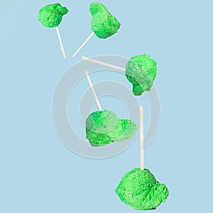A ball of green ice cream on a stick falls and flies through the air until it lands on a flat surface. Pastel blue background