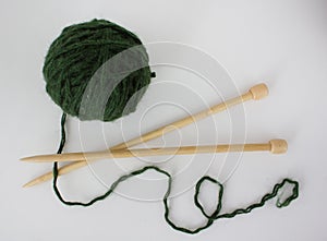 ball of green woolen yarn and two large wooden knitting needles