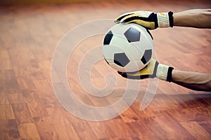 Ball in hands of futsal goalkeeper on wooden futsal floor