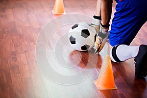 Ball in hands of futsal goalkeeper on wooden futsal floor. Indoor soccer sports hall