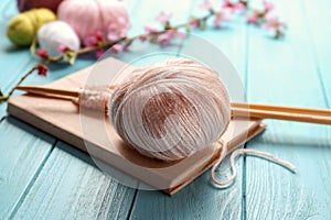 Ball of knitting yarn with needles and book on wooden table