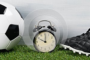 Ball and leather boots for playing football next to the clock on a green background of grass