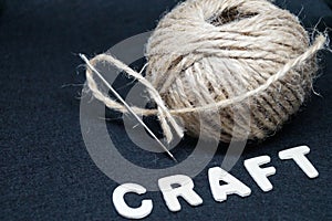 Ball of natural coarse threads with a needle and the inscription wooden craft letters