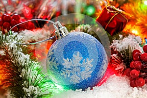 Ball on the snowy branches of a Christmas tree against a background of shiny tinsel. glowing lights