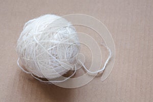 Ball of white wool yarn on cardboard background