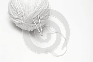ball of white wool yarn with knitting needles on white background