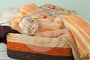 Ball of wool, needles and woolen sweater with spokes for handmade knitting in basket on wooden table.