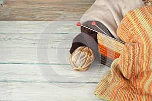 Ball of wool, needles and woolen sweater with spokes for handmade knitting in basket on wooden table