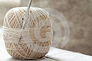 Ball of yarn with crochet hook and beige cotton thread, close-up