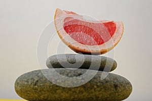 A ballans tower of grey stones and grapefruit orange fruit on a white yellow background with room for text. Benefits of Energy