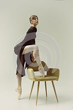 ballerina in a black dress stands showing a deflection and plasticity and putting her foot on a chair