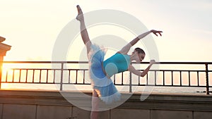 Ballerina in blue ballet tutu and point on embankment above ocean or sea at sunrise. Young beautiful brunette woman