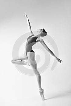 ballerina in a blue bodysuit and ballet shoes poses in a photo studio in motion showing beautiful long legs