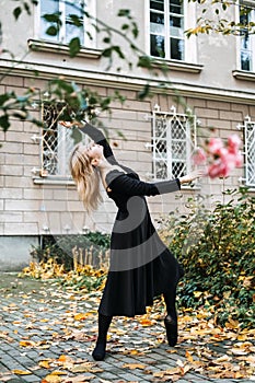 Ballerina Dancing in autumn city street, Modern Ballet Dancer in black dress, Pointe Shoes outdoors. Ballerina stretches