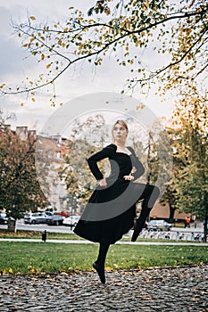 Ballerina Dancing in autumn city street, Modern Ballet Dancer in black dress, Pointe Shoes outdoors. Ballerina stretches